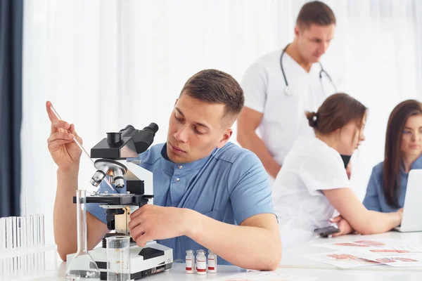 顕微鏡を使う 若い医師のグループが現代のオフィスで一緒に働いています — ストック写真