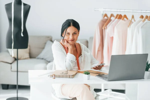 With laptop. Seamstress is in her office that is with different clothes.