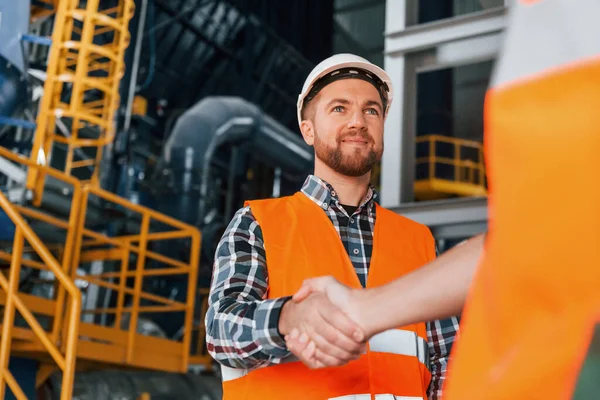 Making handshake with customer. Construction worker in uniform is in the factory.
