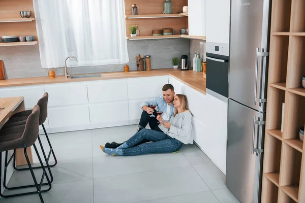 ワインを飲む 現代的なキッチンの床に座っているカップル — ストック写真