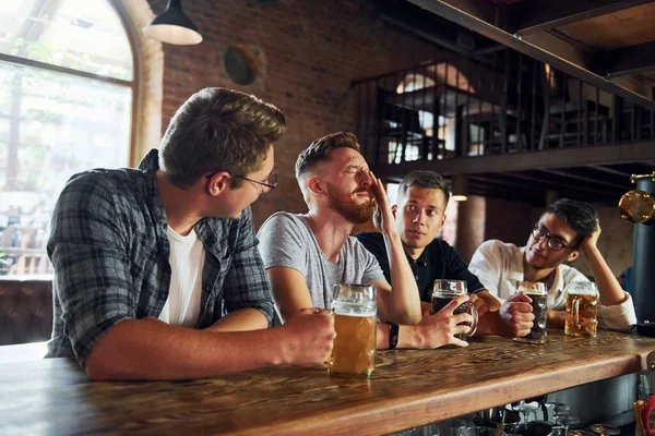 Side view of friends with beer. People in casual clothes sitting in the pub.
