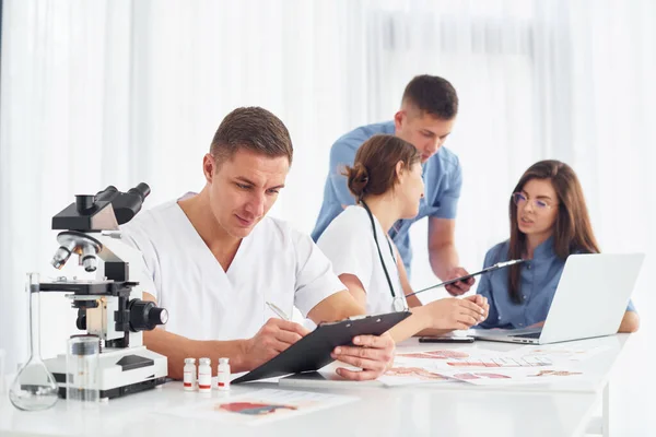 顕微鏡を持った男 若い医師のグループが現代のオフィスで一緒に働いています — ストック写真