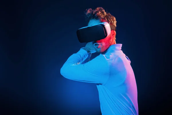 Virtual glasses gaming experience. Neon lighting. Young european man is in the dark studio.