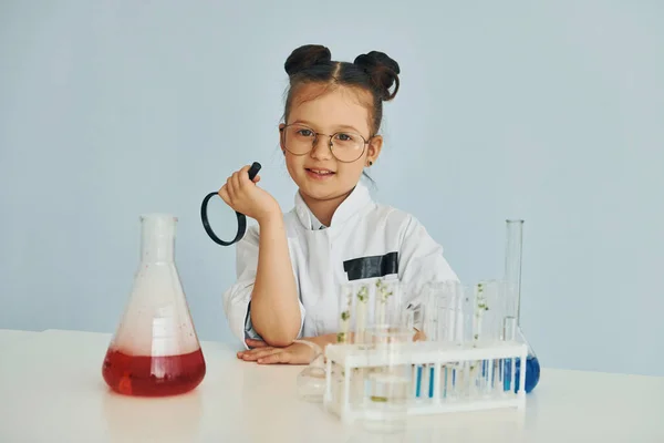 Works with test tubes. Little girl in coat playing a scientist in lab by using equipment.