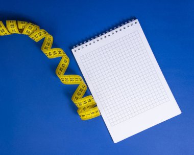 Koyu mavi zemin üzerinde sarı spiral mezura ve defter