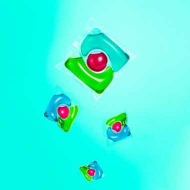 Mavi arkaplanda çok renkli çamaşır yıkamak için jel kapsülünde sıvı tozu