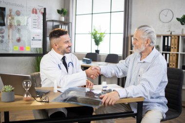 Gülümseyen doktor ve kıdemli hasta ofiste el sıkışıyor.