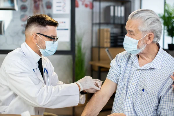 Dokter bertopeng wajah pria melakukan injeksi untuk pasien berusia lanjut. — Stok Foto