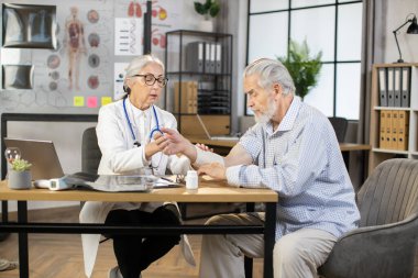 Kadın doktor, yaşlı erkek hastanın yaralı kolunu bandajlıyor.