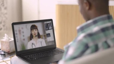 Avrupalı kadın pratisyen hekim, ceket ve kulaklık giyiyor, video aracılığıyla hastaya uzaktan danışmanlık yapıyor.