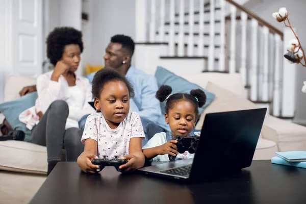 African parents resting on sofa while kids playing on laptop