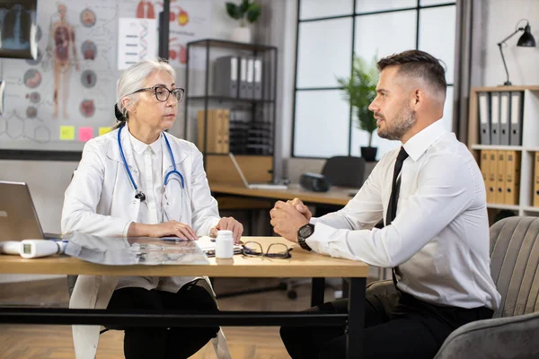 Бизнесмен сидит за столом и разговаривает с семейным врачом — стоковое фото