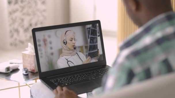 Paciente do sexo masculino com videochamada com seu médico árabe feminino no laptop, segurando varredura de raios X — Vídeo de Stock