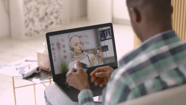 Mulher se senta na frente do laptop com oxímetro de pulso no dedo indicador, conversando com médico árabe on-line — Vídeo de Stock