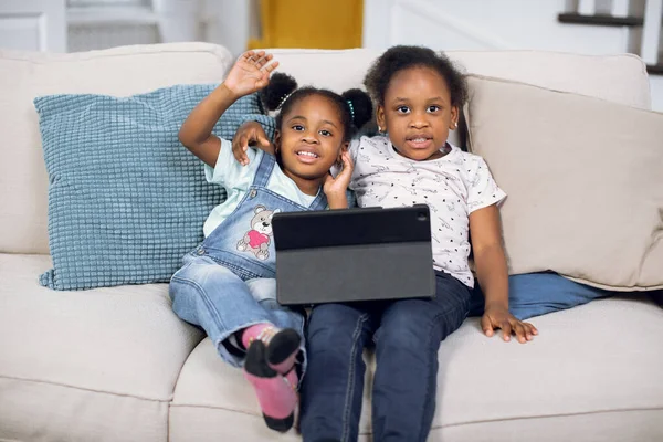 Glimlachen Afrikaans amerikaanse zusters meisjes zitten op de bank met digitale tablet thuis — Stockfoto