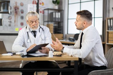 Doktor hasta erkek hastayı dinlerken panoya yazı yazıyor.