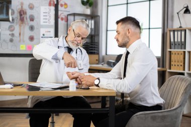 Yaşlı doktor, erkek hastanın sıcaklığını kontrol ediyor.