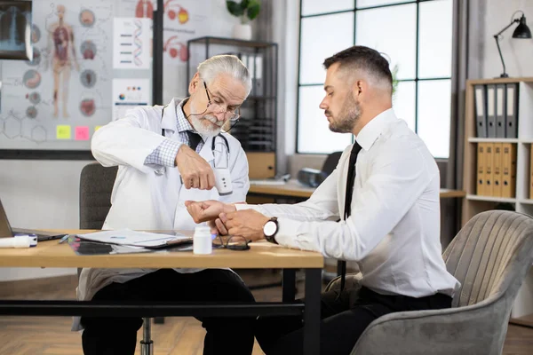 Yaşlı doktor, erkek hastanın sıcaklığını kontrol ediyor.