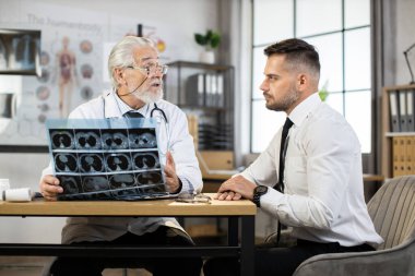 Kıdemli doktor erkek hastaya röntgen sonuçlarını açıklıyor.