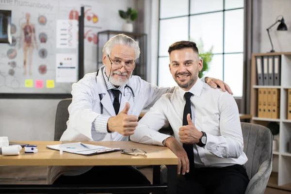 Dokter dan pasien tersenyum dan berpelukan, menunjukkan jempol di kantor medis — Stok Foto