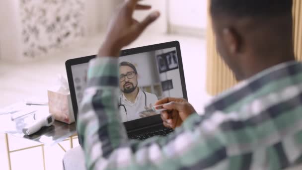 Hombre africano en ropa casual, con termómetro en las manos, teniendo videollamada con médico en el portátil — Vídeos de Stock