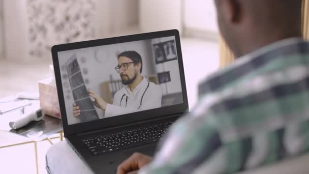 Hombre africano recibiendo videollamada con médico masculino en casa, escuchando tomografía pulmonar resultado de rayos X — Vídeo de stock