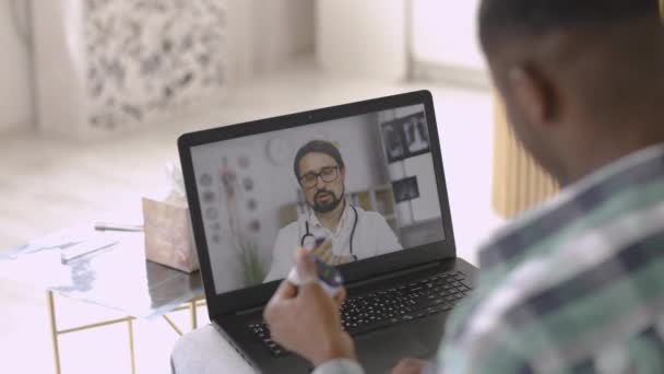 Человек с пульсометром в руках смотрит образовательное видео с врачом-мужчиной на ноутбуке — стоковое видео