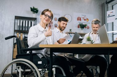 Tekerlekli sandalye kullanan kadın doktor iş arkadaşlarıyla toplantı yapıyor.