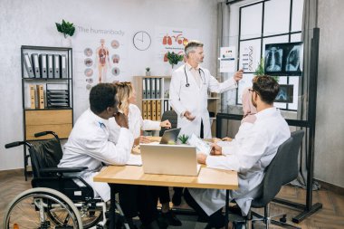 Üniformalı orta yaşlı beyaz doktor DNA teması hakkında uluslararası meslektaşlarına konuşma yapıyor. Çok ırklı tıp uzmanlarından oluşan bir grup konferans sırasında bilgileriyle paylaşıyor.