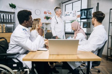 Seminer sırasında uluslararası meslektaşlarıyla birlikte erkek öğretim üyelerini dinleyen Afrikalı Amerikalı bir doktor. Kafkas terapisti toplantı odasında röntgen taramasından bahsediyor..