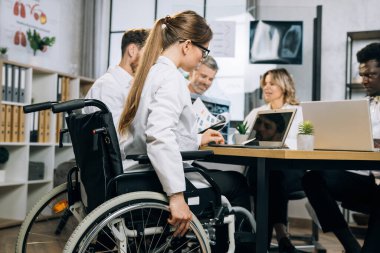 İş birliği için uluslararası meslektaşlarıyla birlikte konferans odasında tekerlekli sandalye toplantısını kullanan beyaz kadın terapist. İnsan kavramı, tıp ve kapsama.
