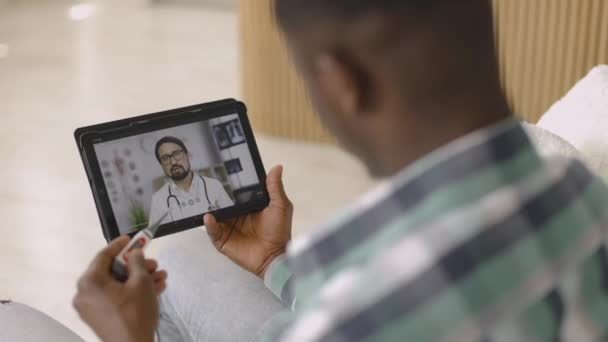 Självsäker manlig läkare som förklarar symtom genom fjärrvideokonferens för sjuk manlig patient — Stockvideo