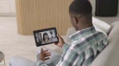 Genç Afrikalı Amerikalı adam, evdeki tablet bilgisayarını kullanarak kadın arkadaşıyla görüntülü konuşma yapıyor.