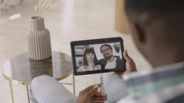 Genç beyaz çift dijital tablet ekranda Afrikalı arkadaşıyla çevrimiçi görüntülü sohbet ediyor.
