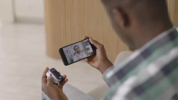 Homme assis avec téléphone portable et tient oxymètre de pouls doigt, ayant chat vidéo avec le médecin masculin — Video