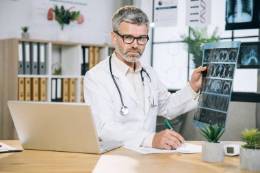 Röntgen taraması yaparken not alan olgun bir doktor.