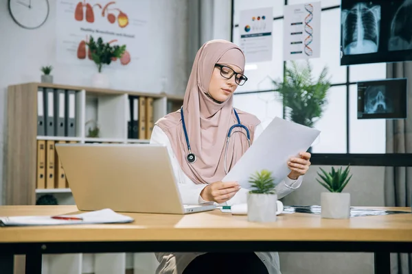 Female therapist in hijab reading documents at office