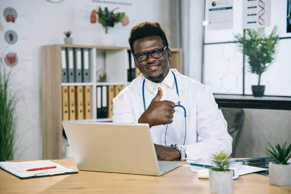 아프리카 계 미국인 의사 사무실에서 일하기 위해 노트북을 사용하는 모습, 엄지손가락을 위로 하고 카메라에 포즈를 취하는 모습 — 스톡 사진
