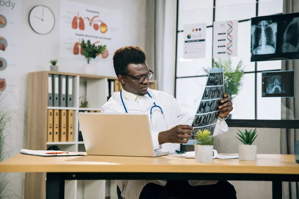 Medico africano in occhiali che tiene la scansione a raggi x alla scrivania — Foto Stock