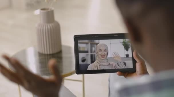 Tablet pc tela com mulher muçulmana, saudação acenando seu amigo masculino Africano via chat de vídeo online — Vídeo de Stock