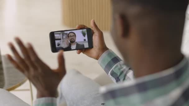 Vue arrière de l'homme africain saluant en webcam du smartphone, tout en ayant un appel vidéo — Video