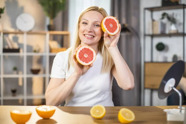Smiling woman holding slices of grapefruit at home — Stock Photo, Image
