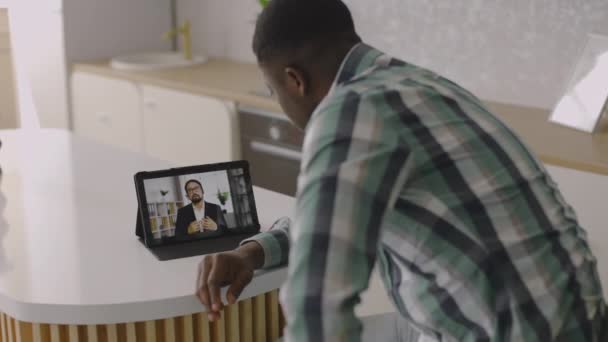 Афроамериканец, сидит за столом на кухне и слушает вебинар онлайн — стоковое видео