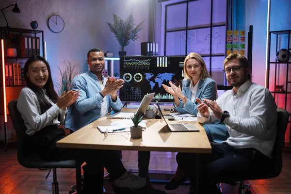 Parceiros multirraciais aplaudindo enquanto estão sentados na mesa do escritório — Fotografia de Stock