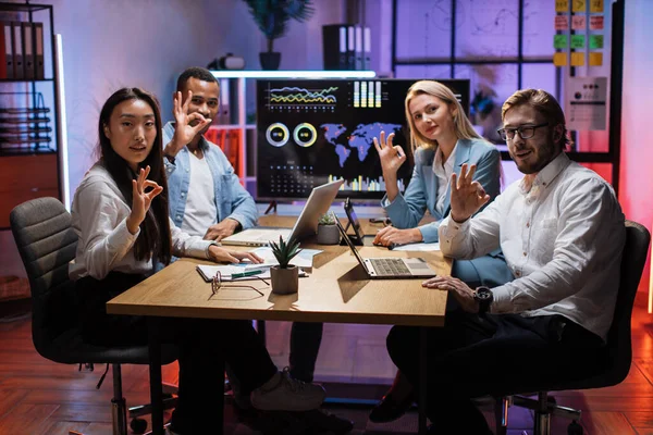 Fyra multietniska kontorsarbetare visar okej skylt på kameran — Stockfoto