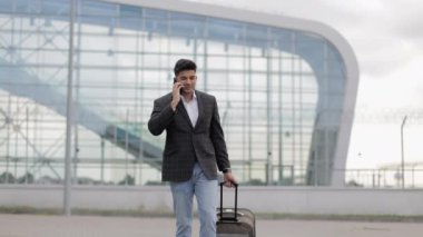 Hintli bir işadamı dışarıda istasyonda ya da havaalanında telefonla konuşuyor ve bavul taşıyor.