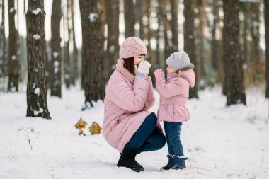 Anne ve küçük tatlı kızı karlı ormanda kış yürüyüşü yapıyorlar. Pembe ceketli anne ve çocuk birbirlerine sevgi ve şefkatle bakıyorlar..