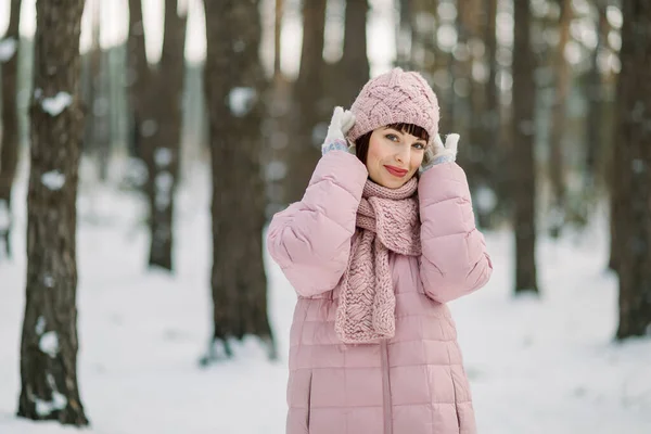 Retrato de inverno ao ar livre de mulher bonita vestindo casaco rosa e chapéu de malha elegante e cachecol, de pé na bela floresta nevada na frente de pinheiros e desfrutar de caminhar no dia gelado. — Fotografia de Stock