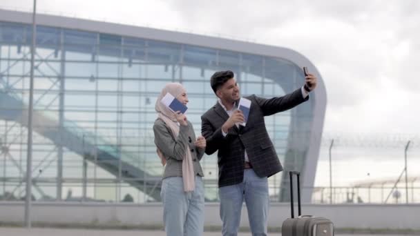 Fröhliches muslimisches Paar macht Selfie im Freien in der Nähe des Flughafenterminals, lächelt glücklich und gestikuliert — Stockvideo