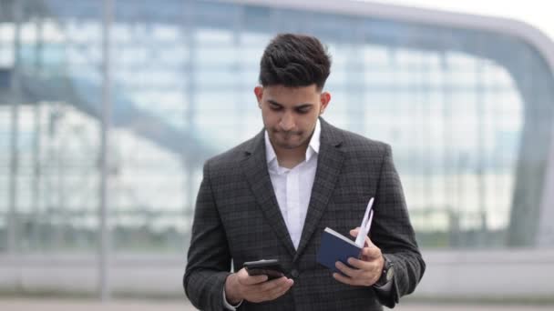 Knappe hindoe met mobiele telefoon, paspoort en instapkaart die zijn vluchtschema controleert. — Stockvideo